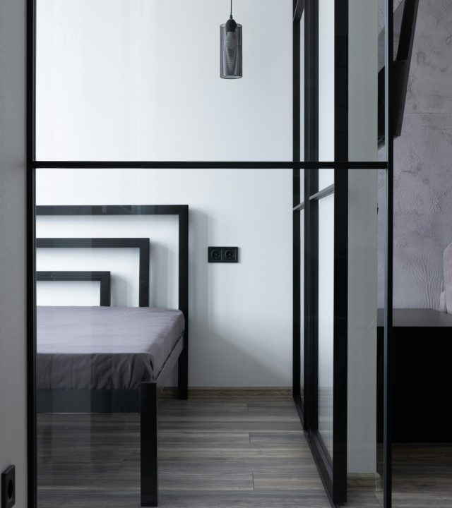 Contemporary bed with mattress and holes in house with hanging lamp and glass division in daytime